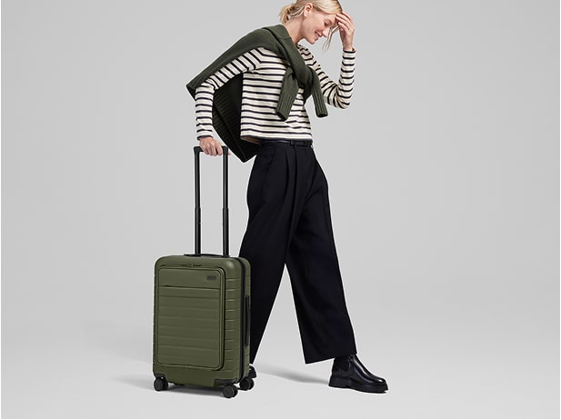 A woman rolling an Away carry-on suitcase in green on a white background