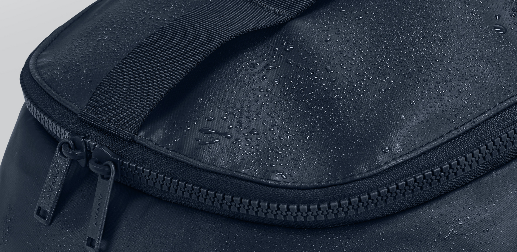 A close up shot of a the top of an Away Active Backpack with water on the outside material showing it's water resistant