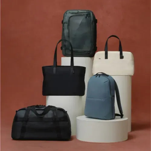 A collection of Away bags, totes, and duffles in various colors on a white background