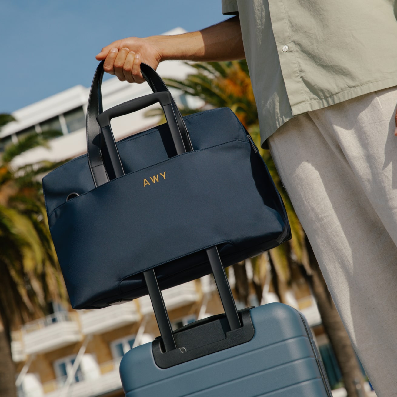 A navy Away duffle with three letters embroidered on the back being held by a man