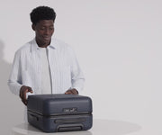 A male model filling The Carry-On suitcase in Navy Blue with Away's packing organizers and using the interior organization and compression system for seamless packing