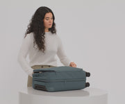 A 5'7" female model filling The Softside Carry-On suitcase in Coast Blue with Away's packing organizers and using the interior organization and compression system for seamless packing