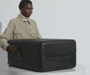 A female model filling The Large suitcase in Jet Black with Away's packing organizers and using the interior organization and compression system for seamless packing